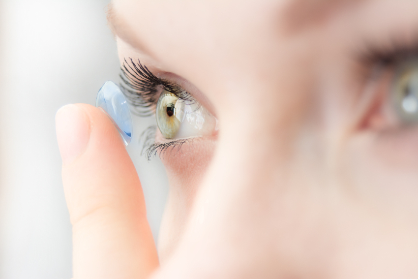 Contact lens exams and specialty fittings A person placing a contact lens on their eye, shown in a close-up view focused on the eye and the lens.