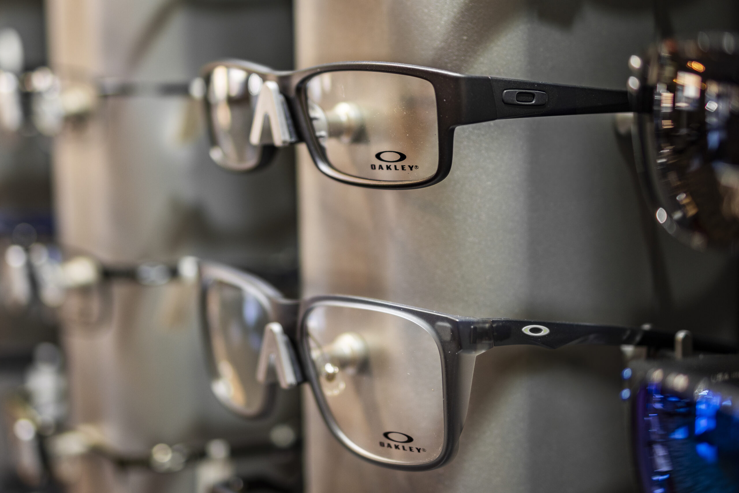 Two pairs of Oakley eyeglasses with black frames are displayed on a shelf, with the Oakley logo visible on the lenses.