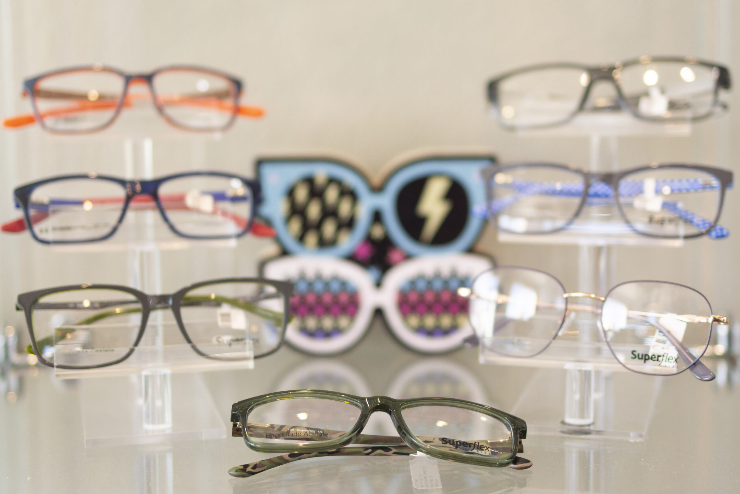 _P5A7995 A display of eight pairs of eyeglasses on clear stands, with a decorative graphic of sunglasses and lightning bolt in the background.