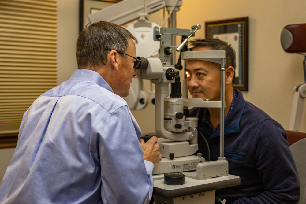 An eye doctor examines a patient's eyes using a slit lamp in an optometrist's office.