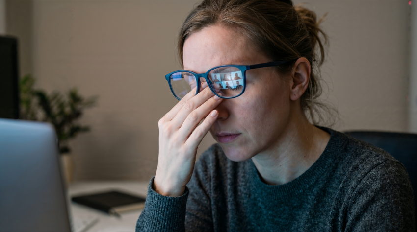 A person wearing glasses sits at a desk, rubbing their eyes while looking at a laptop, appearing tired or stressed—highlighting the importance of pediatric eye care for managing children's vision during screen time.